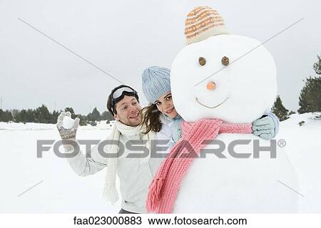 Female embracing snowman and smiling at camera, boyfriend standing behind, holding up snowball View Large Photo Image Stock Image - Female embracing snowman and smiling at camera, boyfriend standing behind, holding up snowball. Fotosearch