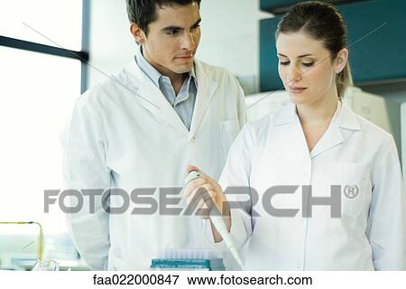 Female lab worker holding dropper, male colleague watching her View Large Photo Image Stock Photo - Female lab worker holding dropper, male colleague watching her. Fotosearch