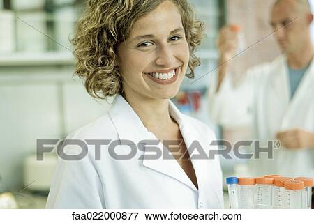 Stock Photo - Female lab worker holding rack of empty test tubes, smiling at camera, portrait. Fotosearch