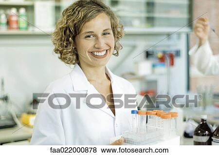 Stock Photo - Female lab worker holding rack of empty test tubes, smiling at camera, portrait. Fotosearch