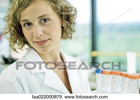 Stock Photo - Female lab worker holding rack of empty test tubes, looking at camera, portrait. Fotosearch