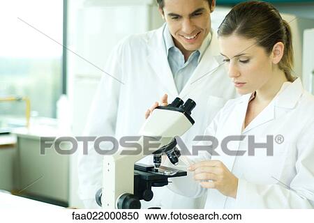 Female lab worker placing slide under microscope, male colleague looking over shoulder, smiling View Large Photo Image Stock Image - Female lab worker placing slide under microscope, male colleague looking over shoulder, smiling. Fotosearch