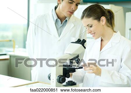 Female lab worker placing slide under microscope, male colleague looking over shoulder View Large Photo Image Stock Image - Female lab worker placing slide under microscope, male colleague looking over shoulder. Fotosearch