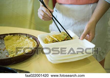 Stock Image - Food service personnel using chopsticks to place food in polystyrene container. Fotosearch