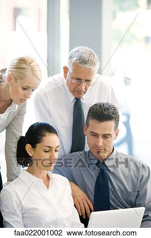 Stock Image - Four business associates looking at laptop computer together. Fotosearch