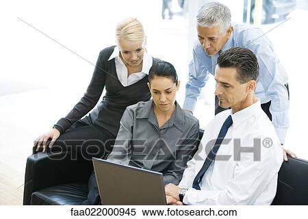 Stock Photography - Four business associates looking at laptop computer together. Fotosearch
