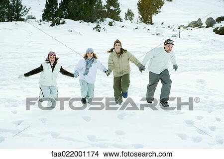 Four young friends running together in snow, holding hands, full length View Large Photo Image Picture - Four young friends running together in snow, holding hands, full length. Fotosearch