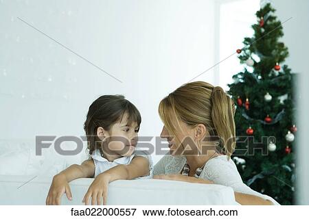 Girl and mother on sofa smiling at each other, Christmas tree in background View Large Photo Image Stock Photo - Girl and mother on sofa smiling at each other, Christmas tree in background. Fotosearch