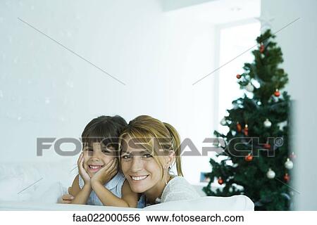 Girl and mother on sofa smiling at camera, Christmas tree in background View Large Photo Image Stock Photograph - Girl and mother on sofa smiling at camera, Christmas tree in background. Fotosearch