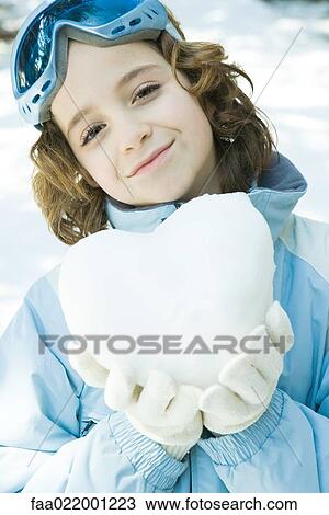 Stock Image - Girl holding heart made of snow, smiling at camera, portrait. Fotosearch