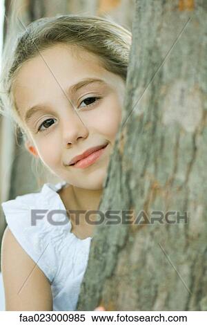 Girl looking around tree trunk at camera, smiling, portrait View Large Photo Image Stock Photography - Girl looking around tree trunk at camera, smiling, portrait. Fotosearch