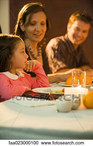 Girl sitting at dinner table with family, looking away View Large Photo Image Stock Image - Girl sitting at dinner table with family, looking away. Fotosearch