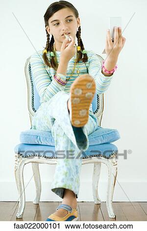 Stock Image - Girl sitting in chair, putting on make-up. Fotosearch