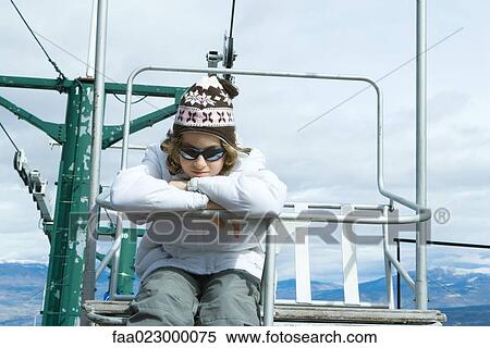 Stock Photography - Girl sitting on chair lift, head resting on arms, looking at camera. Fotosearch