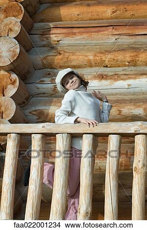 Picture - Girl standing on deck of wood cabin, striking a pose. Fotosearch