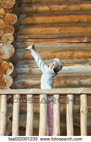 Stock Image - Girl standing on deck of wood cabin, stretching arms. Fotosearch