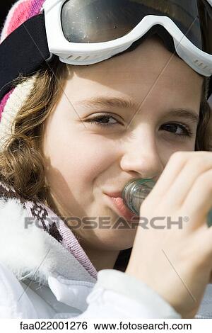 Stock Photograph - Girl wearing ski gear, drinking from bottle, close-up. Fotosearch