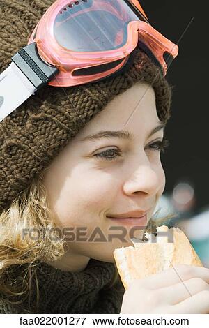 Stock Photo - Girl wearing ski gear, eating sandwich, close-up. Fotosearch