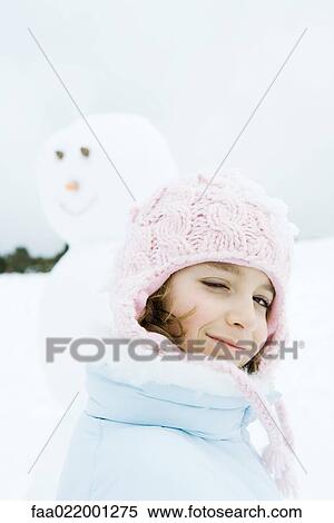 Stock Photography - Girl winking at camera, snowman in background. Fotosearch