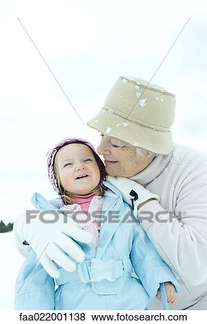 Stock Photo - Grandmother embracing toddler in snow, both smiling. Fotosearch
