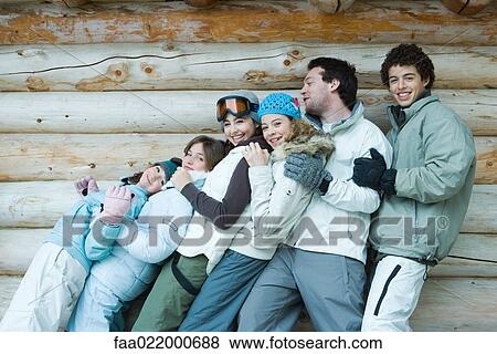 Stock Photo - Group in winter clothes falling back onto each other, three quarter length, in front of log wall, portrait. Fotosearch