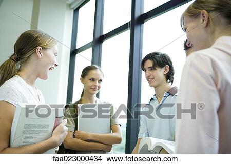 Picture - Group of college students standing around, holding books and binders, chatting. Fotosearch