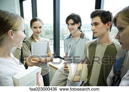 Group of college students standing around, holding books and binders, chatting View Large Photo Image Stock Photograph - Group of college students standing around, holding books and binders, chatting. Fotosearch