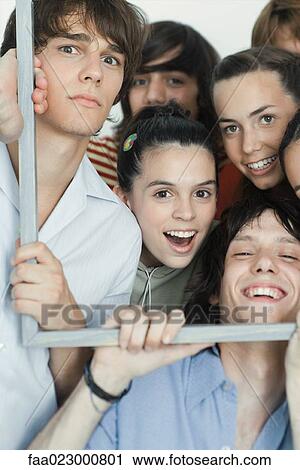 Stock Image - Group of young friends posing for photo, holding up picture frame, looking at camera, portrait. Fotosearch