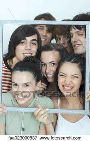Stock Photo - Group of young friends posing for photo, holding up picture frame, smiling at camera, portrait. Fotosearch