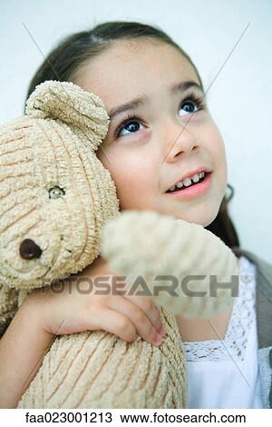 Stock Image - Little girl holding teddy bear, looking up, portrait. Fotosearch