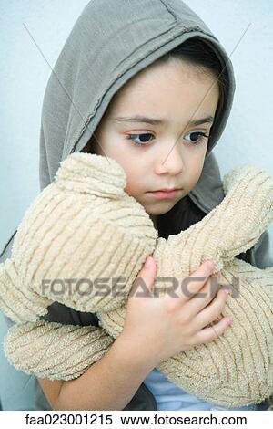 Stock Photography - Little girl holding teddy bear, looking down, portrait. Fotosearch