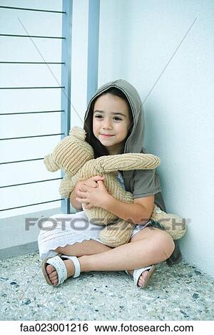 Stock Photograph - Little girl sitting on floor, holding teddy bear, smiling, full length. Fotosearch