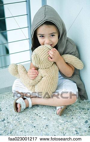 Stock Photo - Little girl sitting on floor, whispering into teddy bear's ear, full length. Fotosearch