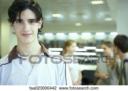 Male college student in library, smiling at camera, other students chatting in blurred background View Large Photo Image Stock Image - Male college student in library, smiling at camera, other students chatting in blurred background. Fotosearch