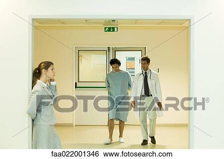 Male doctor and patient walking together in hospital corridor, woman using cell phone in foreground View Large Photo Image Stock Photograph - Male doctor and patient walking together in hospital corridor, woman using cell phone in foreground. Fotosearch