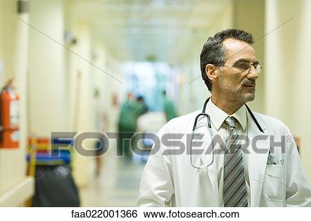 Stock Photograph - Male doctor looking away, hospital corridor in background. Fotosearch