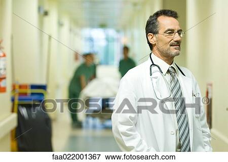 Stock Photo - Male doctor looking away, smiling, hospital corridor in background. Fotosearch