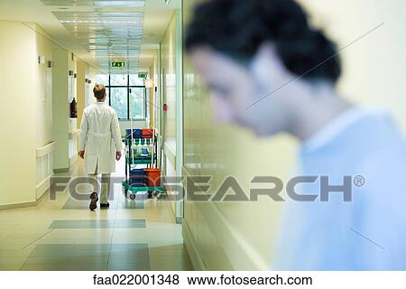 Stock Photo - Male doctor walking in hospital corridor, rear view, man with head down in foreground. Fotosearch
