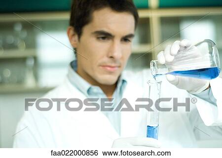 Stock Photograph - Male lab worker transferring solution from flask to graduated cylinder. Fotosearch