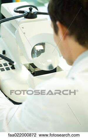 Stock Image - Male lab worker using lab machine, rear view. Fotosearch