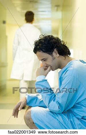 Male patient crouching in hospital corridor, holding head, looking down, doctor walking away in background View Large Photo Image Stock Photo - Male patient crouching in hospital corridor, holding head, looking down, doctor walking away in background. Fotosearch