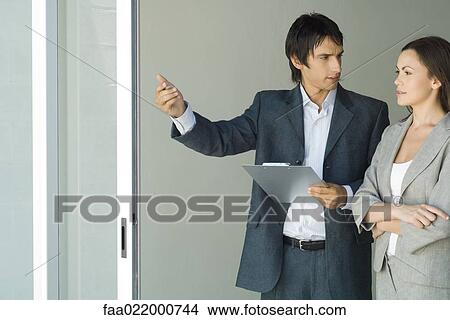 Picture - Male real estate agent showing house to female client, standing by sliding glass door, woman looking out, smiling. Fotosearch