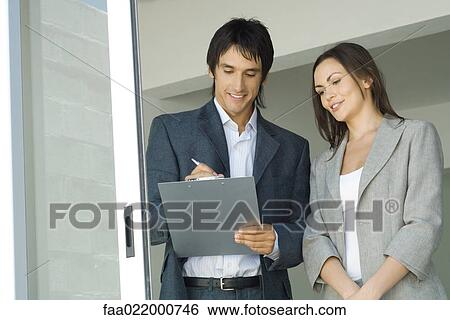 Male real estate agent showing house to female client, writing on clipboard View Large Photo Image Stock Photograph - Male real estate agent showing house to female client, writing on clipboard. Fotosearch