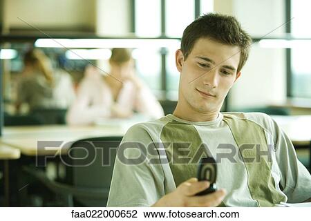 Male student checking cell phone in library study area View Large Photo Image Stock Image - Male student checking cell phone in library study area. Fotosearch