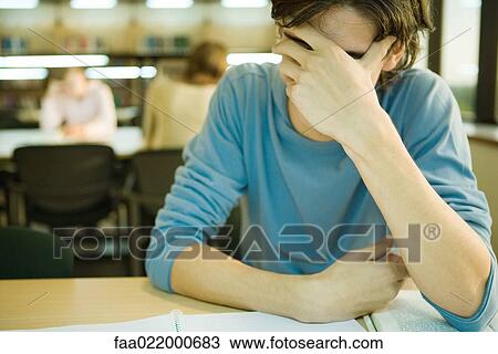 Stock Image - Male student in library covering face. Fotosearch
