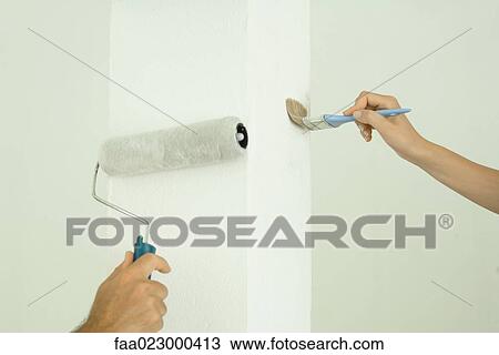 Stock Image - Man and woman painting with paintbrush and roller, close-up of hands. Fotosearch