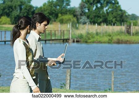 Man and woman standing by lake, man holding laptop View Large Photo Image Stock Photo - Man and woman standing by lake, man holding laptop. Fotosearch