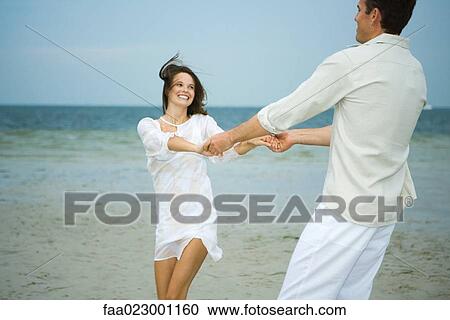 Man and young female companion on beach, holding hands, swinging each other around View Large Photo Image Stock Image - Man and young female companion on beach, holding hands, swinging each other around. Fotosearch