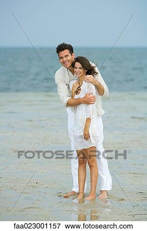 Man and young female companion on beach, standing together, looking at camera, full length View Large Photo Image Stock Photo - Man and young female companion on beach, standing together, looking at camera, full length. Fotosearch