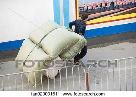 Stock Image - Man carting cushions through street, China, Guangdong Province, Guangzhou.. Fotosearch